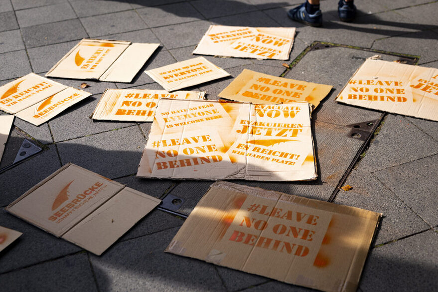 Mehrere beschriftete Schilder mit dem Slogan "Leave no one behind" liegen auf dem Boden.