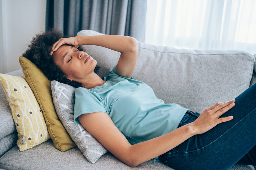 Eine Frau sitzt mit geschlossenen Augen müde auf dem Sofa.
