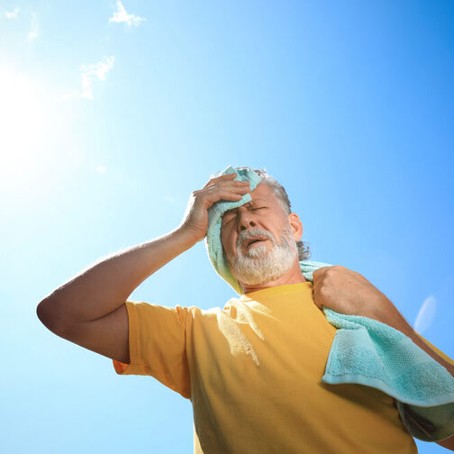 Ein älterer Mann, der sich mit einem Handtuch die Stirn abwischt, leidet unter der Hitze