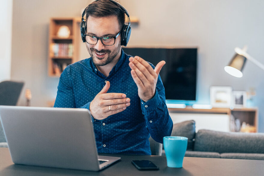 Ein Mann sitzt mit Kopfhörern vor einem Laptop und ist in einer Online-Konferenz.