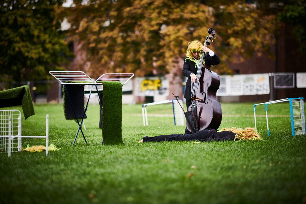 Ein Cellist spielt im Park der Villa Berg. Neben ihm ein Wäscheständer mit Rasenbahnen