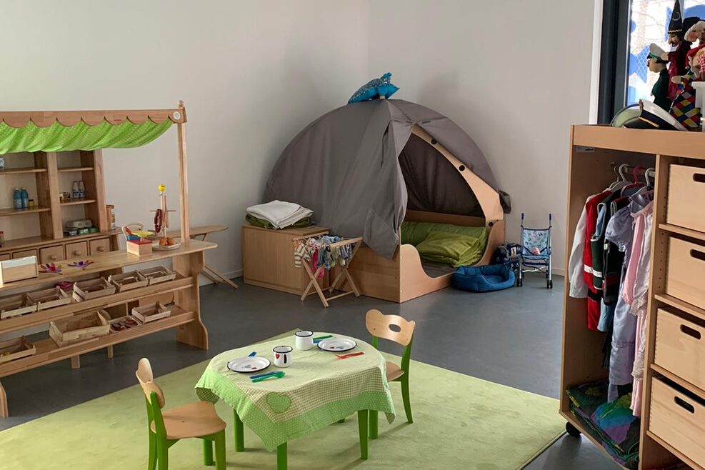Rollenspielzimmer mit Kaufladen, Tisch, Zelt und Kleiderschrank zum Spielen für Kinder.
