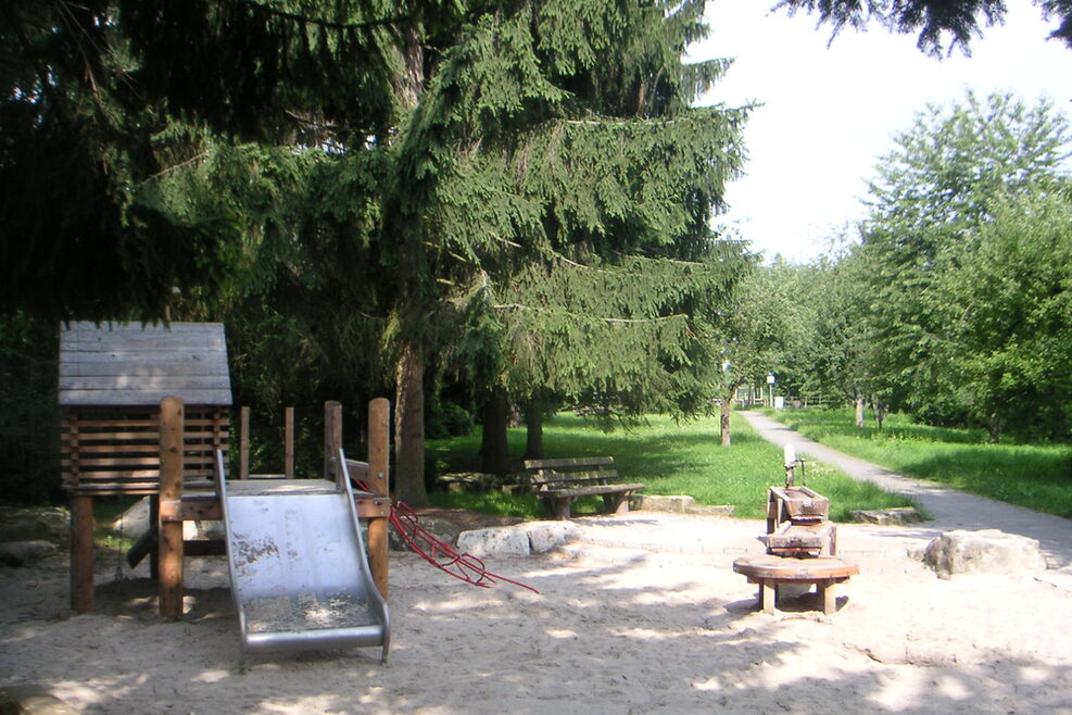 Der Spielplatz im Außenbereich hat einen großen Sandkasten mit Wasserstraße und ein Klettergerüst mit breiter Rutsche.