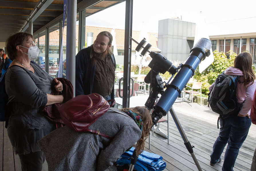 Auf der Dachterasse des Rathauses schaut eine Frau durch ein Teleskop. Links daneben steht ein Mann und unterhält sich mit einer weiteren Frau.