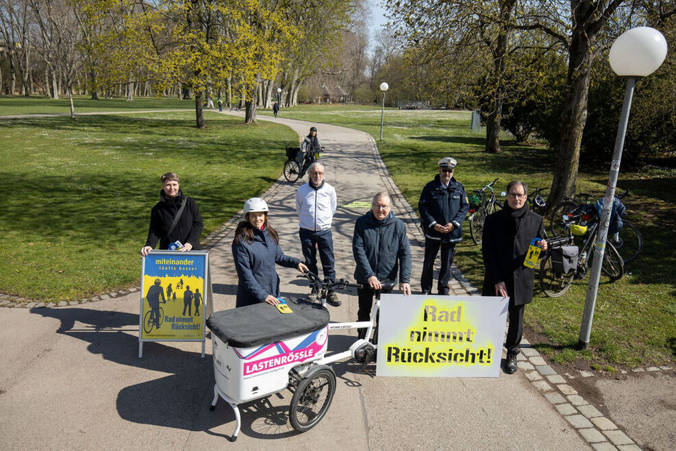 Ein Plakat mit der Aufschrift "Rad nimmt Rücksicht" steht auf einem Fußweg, im Hintergrund nähert sich eine Radfahrerin.