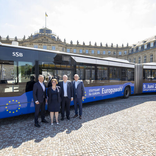 Ein Bus der SSB im Ehrenhof des Neuen Schloss. Der Bus ist mit einem Wahlaufruf zur Europawahl beklebt. Vor dem Bus stehen vier Personen.