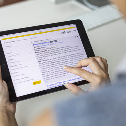 Eine Person hält ein Tablet in den Händen. Auf dem Display ist die Startseite der Online-Freiwilligenbörse zu sehen.