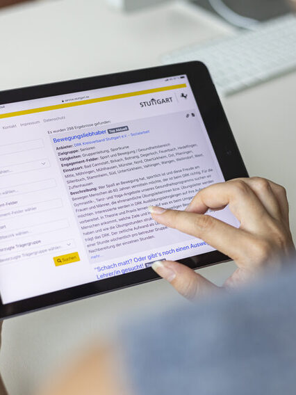 Eine Person hält ein Tablet in den Händen. Auf dem Display ist die Startseite der Online-Freiwilligenbörse zu sehen.