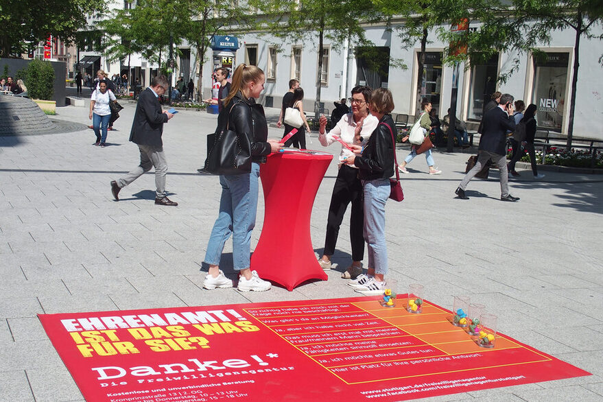 Eine Frau berät zwei Passantinnen in der Fußgängerzone über Ehrenamt.