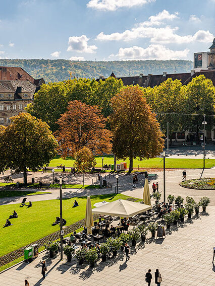 Auf dem Bild ist der Schlossplatz Stuttgart mit dem Alten Schloss zu sehen. Das Wetter ist schön, die Sonne scheint. Zu sehen sind Menschen, die flanieren.