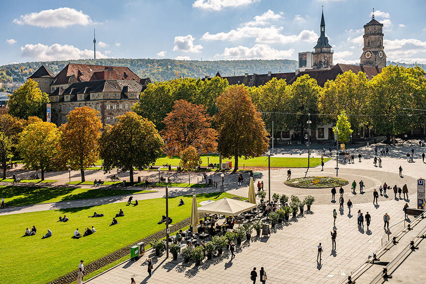 Auf dem Bild ist der Schlossplatz Stuttgart mit dem Alten Schloss zu sehen. Das Wetter ist schön, die Sonne scheint. Zu sehen sind Menschen, die flanieren.