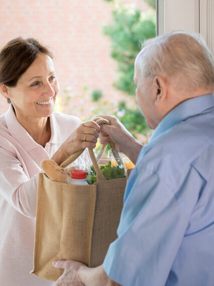 Eine Frau überreicht einem älteren Mann eine Tasche voller Lebensmittel.