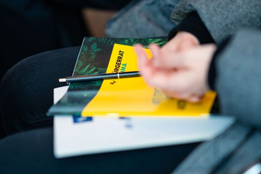 Foto aus der ersten Sitzung des Bürgerrat Klima am 18. März 2023. Zu sehen ist eine Broschüre mit Stift einer Teilnehmerin im großen Sitzungssaal des Rathaus in Stuttgart.