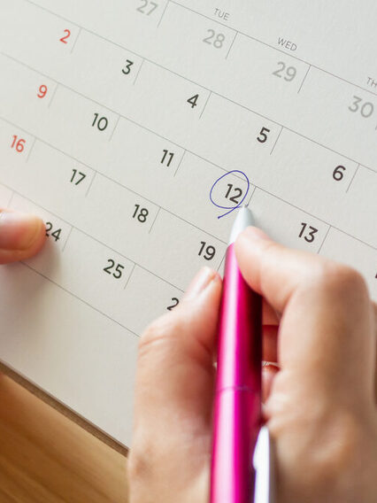 Eine Hand markiert mit einem Stift einen Tag im Kalender