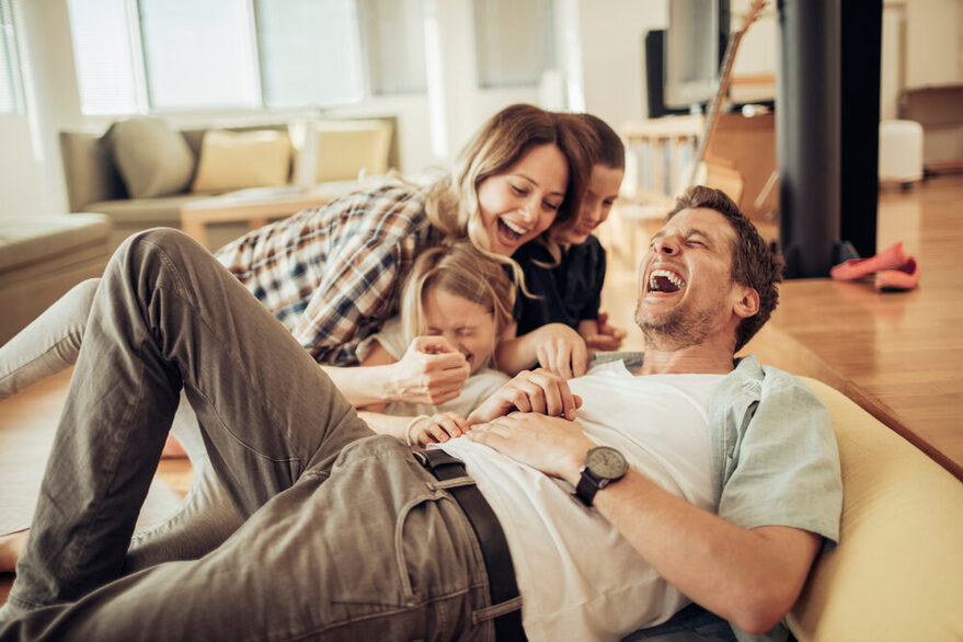 Junge Familie lacht im Wohnzimmer.