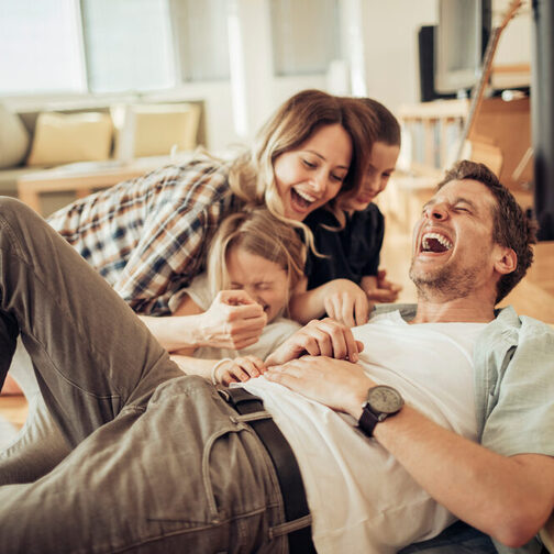 Junge Familie lacht im Wohnzimmer.