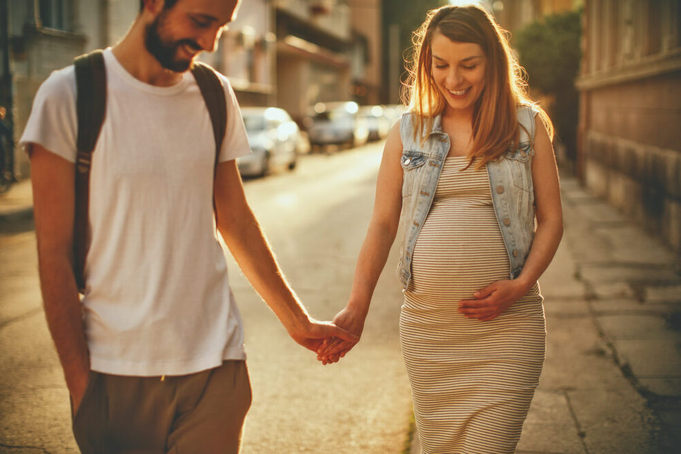 Schwangere Frau und Partner beim Spaziergang in der Stadt.
