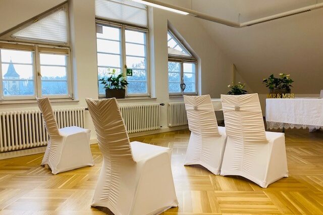 Blick in einen Raum, in dem Stühle mit weißen Hussen stehen.