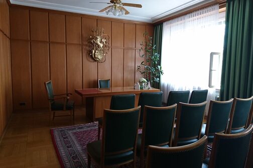 Blick in einen Raum mit Holzvertäfelung und grünen Stühlen.