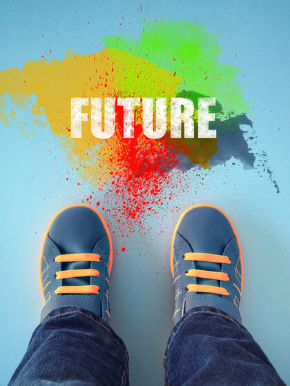 Blick auf zwei Kinderfüße, die vor einem bunten Farbklecks stehen. In dem Klecks steht „Future“ (Zukunft).