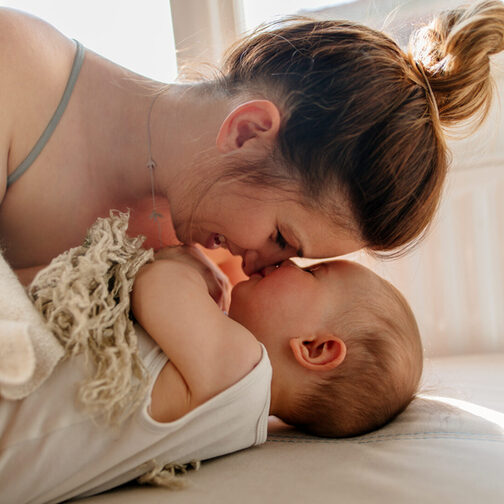 Eine Frau liegt mit einem Baby auf einem Bett und kuschelt.