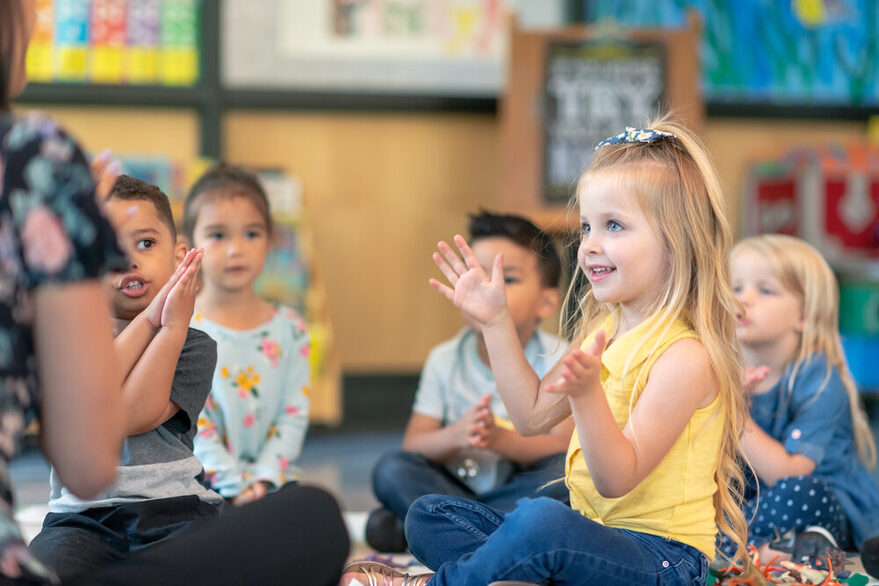 Mehrere Kinder sitzen auf dem Boden und klatschen zusammen mit einer Erzieherin.