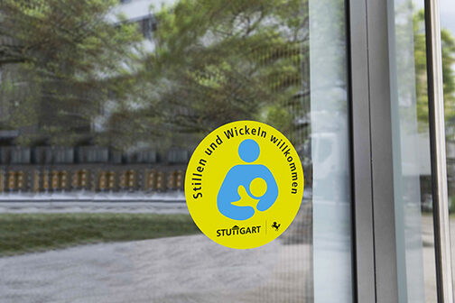 Ein Aufkleber mit der Aufschrift Stillen und Wickeln willkommen und einem Piktogramm von einer stillenden Person klebt auf einer Eingangstür.