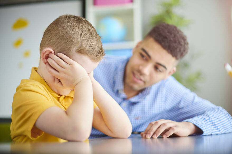 Ein Mann spricht mit einem Jungen, der sein Gesicht in den Händen versteckt.