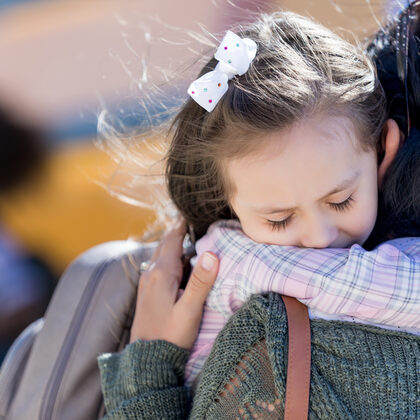 Ein kleines Mädchen mit weißer Schleife im Haar umarmt eine Frau.