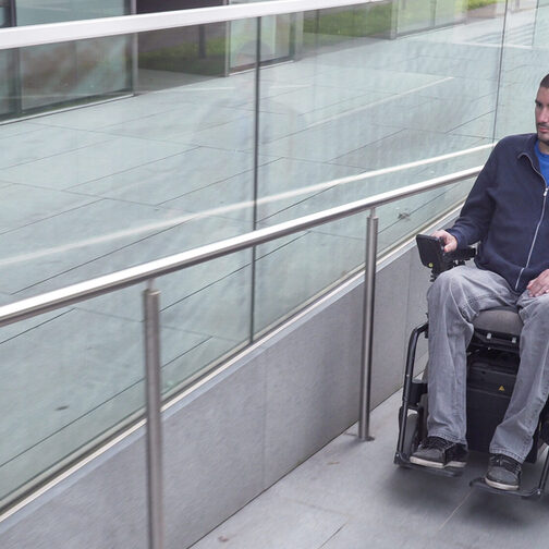 Ein Mann sitzt in einem elektrischen Rollstuhl und fährt eine Rampe hinauf.