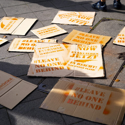 Mehrere beschriftete Schilder mit dem Slogan "Leave no one behind" liegen auf dem Boden.