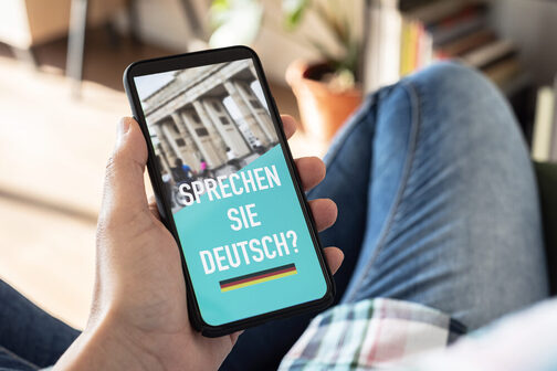 Ein Hand hält ein Smartphone. Auf Bildschirm steht "Sprechen Sie Deutsch?"