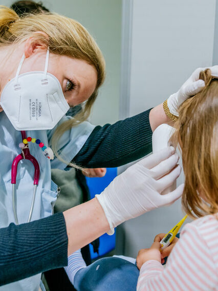 Eine Ärztin mit Maske im Gesicht untersucht ein Kind.