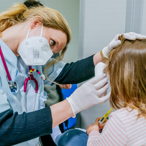 Eine Ärztin mit Maske im Gesicht untersucht ein Kind.