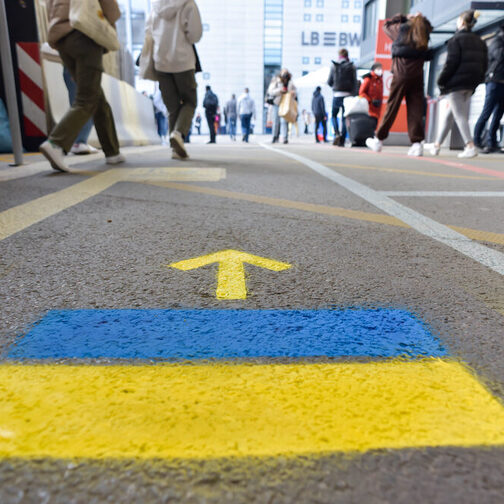 Wegweiser am Hauptbahnhof Stuttgart für Menschen aus Ukraine, zwei Farbstreifen in blau und gelb mit einem Pfeil