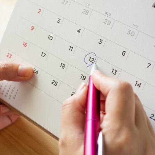 Kalender: Eine Hand kreist mit einem Kugelschreiber einen Tag ein.
