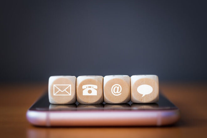 Nahaufnahme eines Telefon-, E-Mail-, Chat- und Post-Symbols aus Holzwürfeln, die in einer Reihe auf einem Mobiltelefon angeordnet sind.