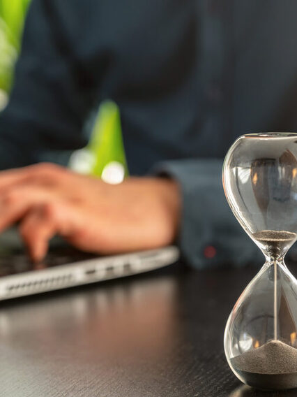 Ablaufende Sanduhr auf dem Schreibtisch als Symbol für Zeitdruck oder ablaufende Fristen