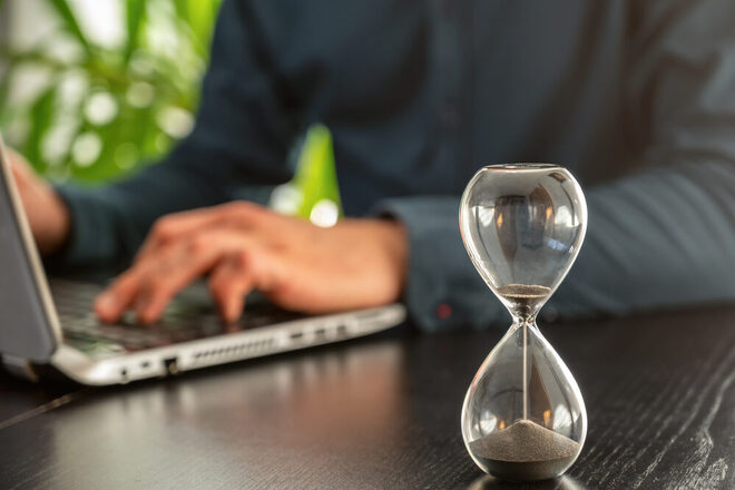 Ablaufende Sanduhr auf dem Schreibtisch als Symbol für Zeitdruck oder ablaufende Fristen