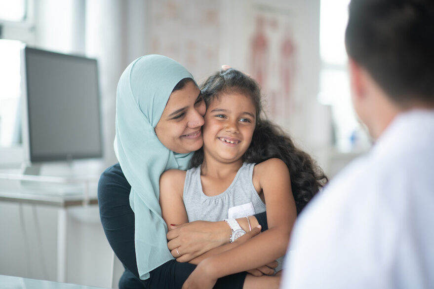 Eine muslimische Mutter mit ihrer Tochter sitzt in einer Arztraxis vor einem Arzt.