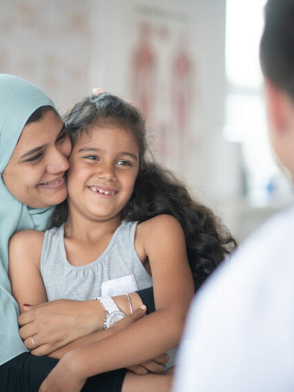 Eine muslimische Mutter mit ihrer Tochter sitzt in einer Arztraxis vor einem Arzt.