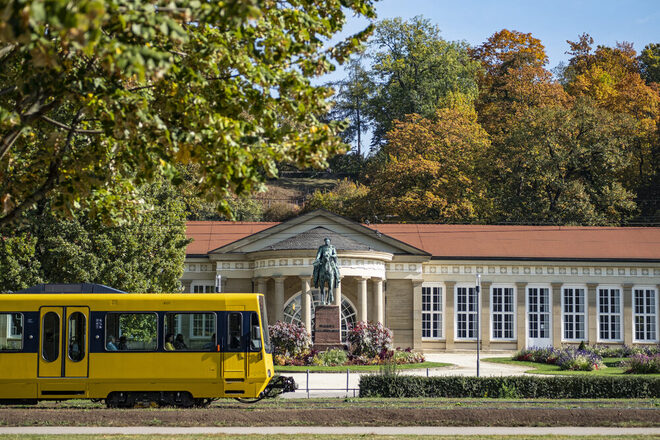 Eine gelbe Stadtbahn fährt am Kurpark vorbei.
