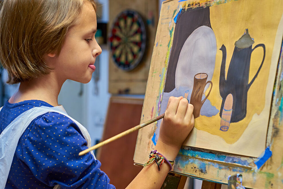 Junges Mädchen malt konzentriert auf einer Leinwand ein buntes Bild.