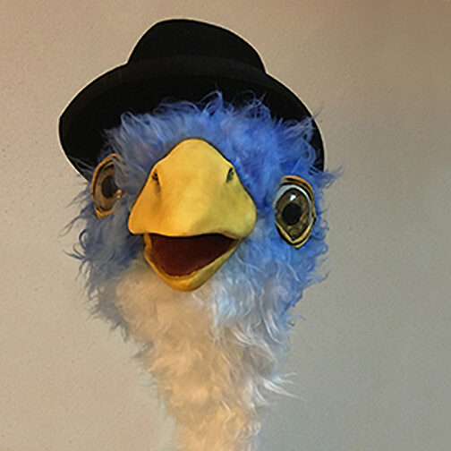 Porträt des Maskottchens der Stuttgarter Philharmoniker: Vogelpuppe mit blauem Kopf und gelbem Schnabel, einen Hut tragend