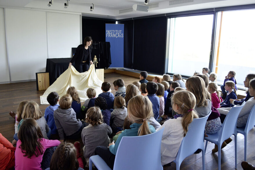 Mehrere Kinder schauen einer Frau zu, die etwas vorträgt.