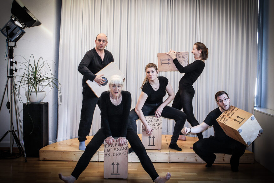 Fünf Menschen in schwarzer Kleidung performen mit Kisten auf einer Bühne.