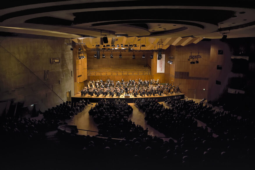 Konzertraum mit Orchester und Zuschauern.