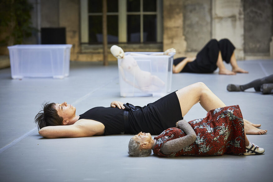 Performance-Darstellerinnen liegen mit Menschenpuppen auf dem Boden.