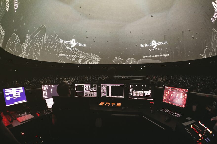 Menschen mit Smartphones in der Hand unter der Sternenkuppel im Planetarium.