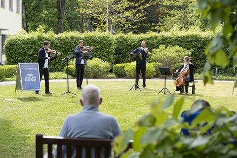 Musikerinnen spielen in einem Garten, ein Mann hört zu.